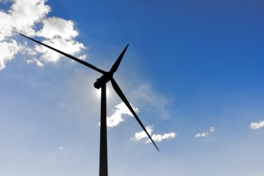 Wind turbine in the back light of the sun with blue sky and clou clipart