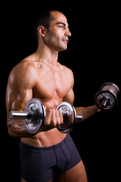 Muskulöser junger Mann hebt Hanteln auf schwarzem Hintergrund. — Stockfoto