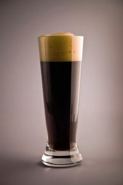 Kieliszek ciemnego piwa z piany na szarym tle — Zdjęcie stockowe