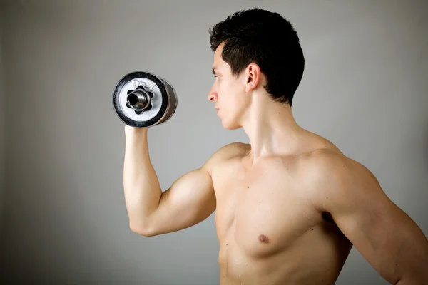 Starker junger Mann hebt Gewicht vor grauem Hintergrund — Stockfoto
