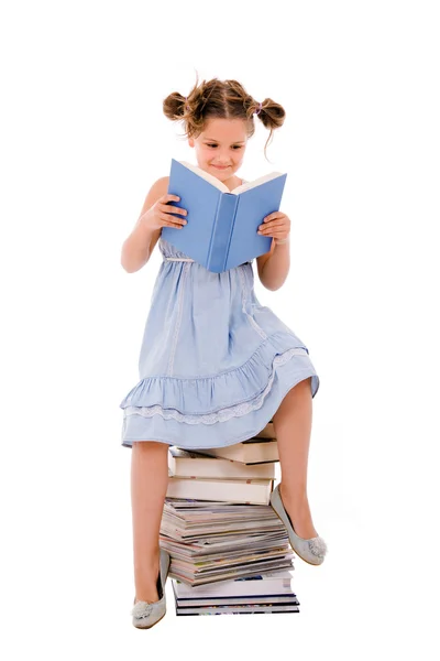 Imagen de colegiala sentada en el montón de libros y leyendo uno — Foto de Stock