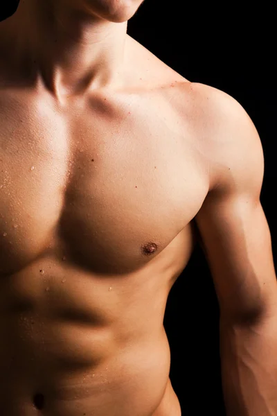 Junger Mann mit nacktem muskulösen Oberkörper vor schwarzem Hintergrund — Stockfoto