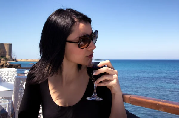 Красивая молодая женщина пьет красное вино у моря — стоковое фото