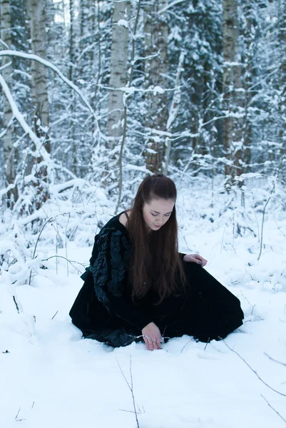 Schoonheid meisje in zwarte jurk zitten in winter forest — Stockfoto