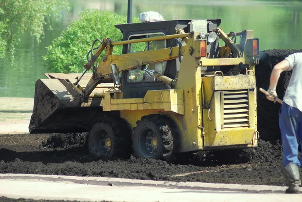 Mini excavadora-agarre de trabajo en el parque de la ciudad en la primavera —  Fotos de Stock