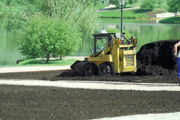 Mini excavadora-agarre de trabajo en el parque de la ciudad en la primavera — Foto de Stock
