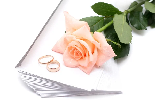 Rosa, sobres y anillos de boda sobre un fondo blanco Fotos de stock libres de derechos