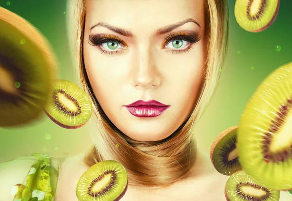 Mooie blonde vrouw met kiwi op groene achtergrond — Stockfoto