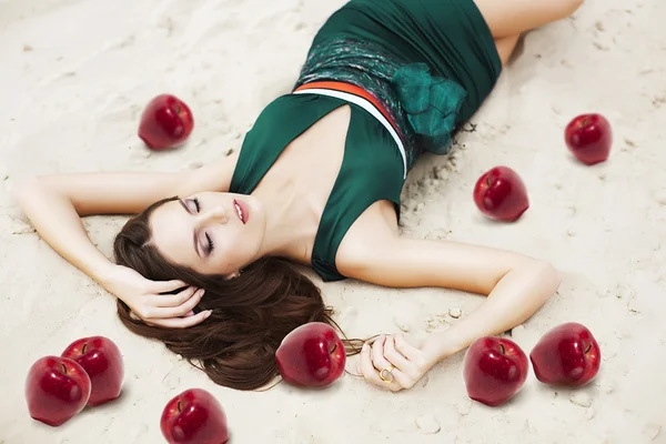 Kvinna med röda äpplen på sanden i grön klänning — Stockfoto