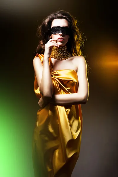 Чувственная взрослая женщина в золотом платье и черной маске — стоковое фото