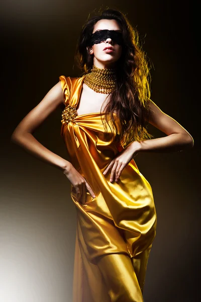 Sensuele volwassen vrouw in een gouden jurk en masker — Stockfoto