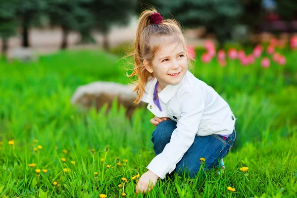 Doce menina bonita sentada em um prado verde — Fotografia de Stock