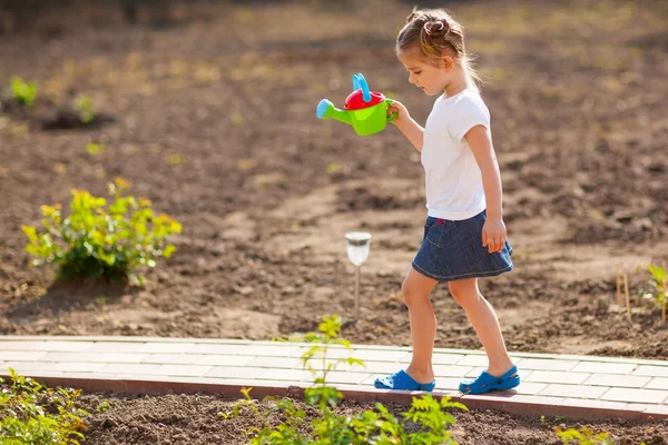 Klein meisje water geven bloemen in de tuin — Stockfoto