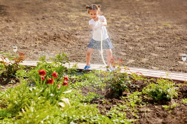 Mała dziewczynka podlewanie kwiaty w ogrodzie — Zdjęcie stockowe