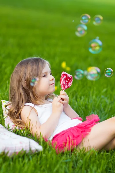 Cute child with lollipop resting on the grass — Stock Photo, Image