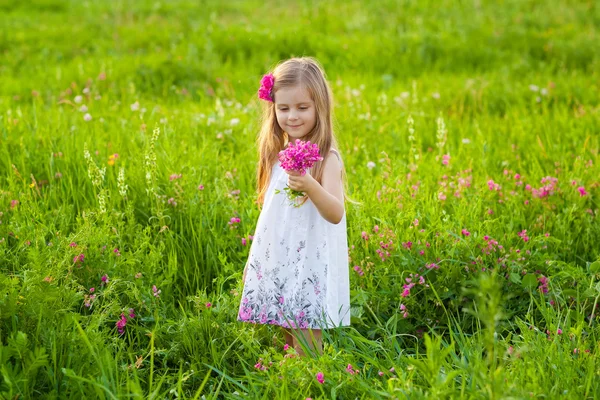 Doce menina loira cheirando flores no prado — Fotografia de Stock