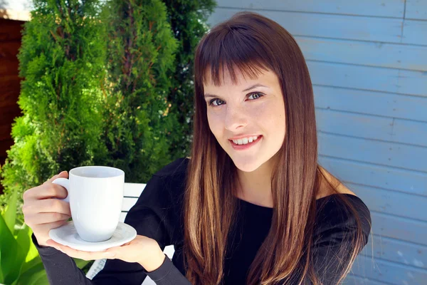 Девушка, держащая чашку кофе и приятно улыбаясь — стоковое фото