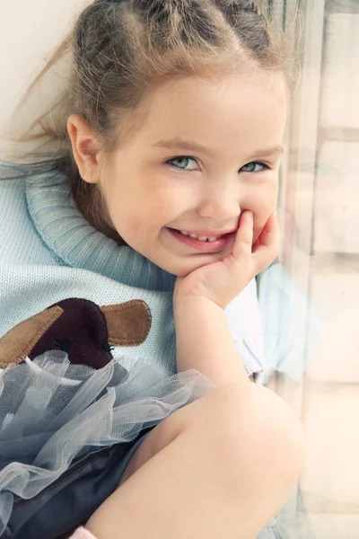Κορίτσι παιδί κάθεται στο παράθυρο και χαμογελαστός — Φωτογραφία Αρχείου