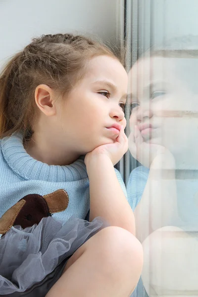 Menina sentada no peitoril da janela e olhando pela janela — Fotografia de Stock