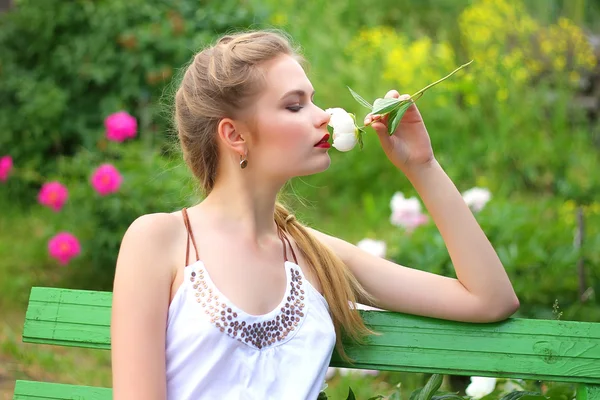 Ładna dziewczyna w ogrodzie na ławce z białych kwiatów w Witam — Zdjęcie stockowe