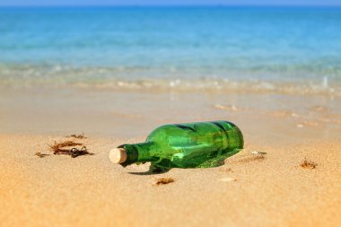 Green glass bottle with a letter thrown out on a sandy beach clipart