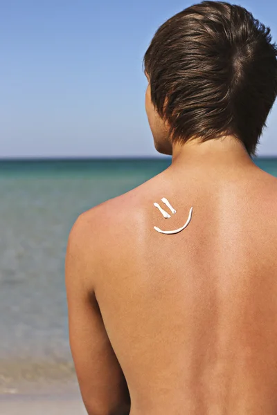 Il ragazzo seduto sulla spiaggia con un sorriso di crema solare sul suo s — Foto Stock