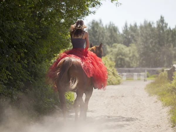 A girl in a red skirt rides a horse — Stock Photo, Image