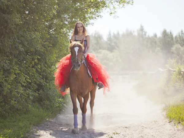 Une fille en jupe rouge monte à cheval — Photo
