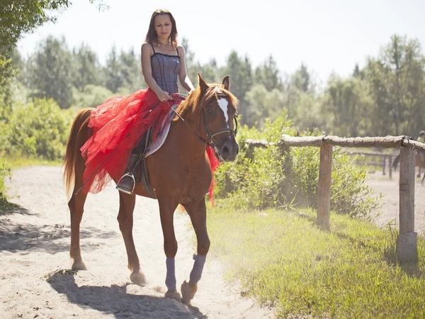 A girl in a red skirt sitting on a horse — Stock Photo, Image