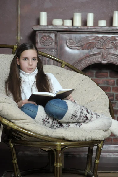 Tenåringsjente leser en bok mens hun sitter i en stol – stockfoto