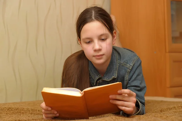 La ragazza l'adolescente legge il libro sdraiato su un divano — Foto Stock