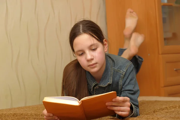 A menina o adolescente lê o livro deitado em um sofá — Fotografia de Stock