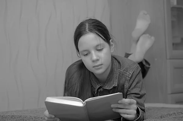 Девочка-подросток читает книгу, лежащую на диване — стоковое фото