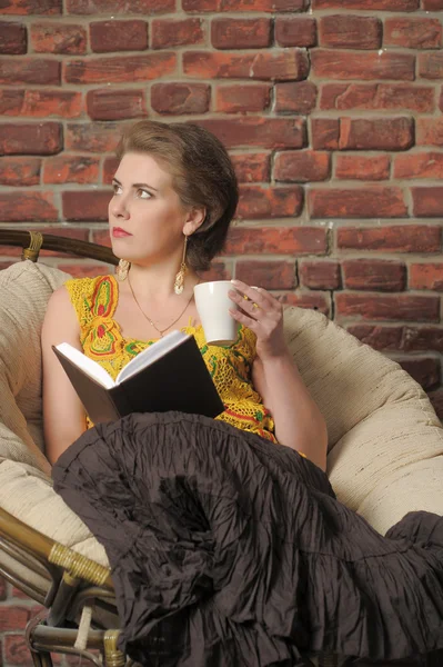 本と椅子にカップを持つ女性. — ストック写真