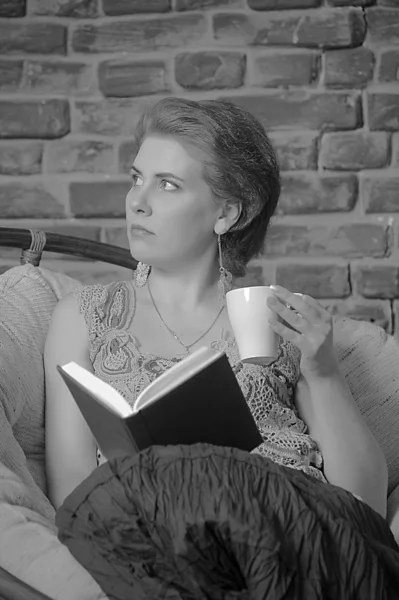 Mujer con un libro y una taza en la silla . —  Fotos de Stock