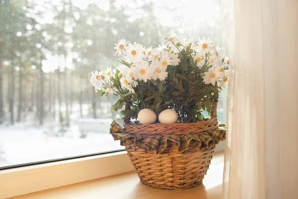Huevos blancos están en una cesta con flores en un alféizar de la ventana en la casa Fotos de stock