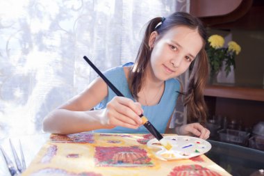 Positive schoold girl are painting at home clipart