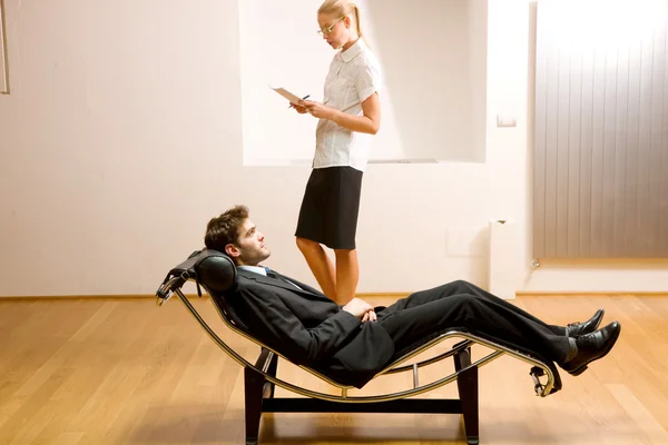 Woman reading man lying on chaise longue — Stock Photo, Image