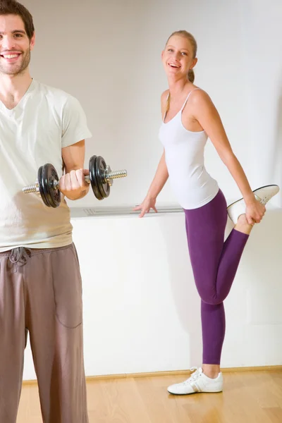 Mann hebt Hantel und Frau dehnt sich im Fitnessstudio — Stockfoto
