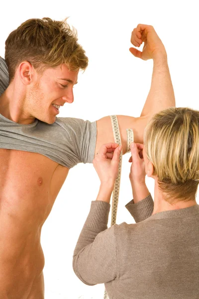 Mujer midiendo bíceps de un joven — Foto de Stock
