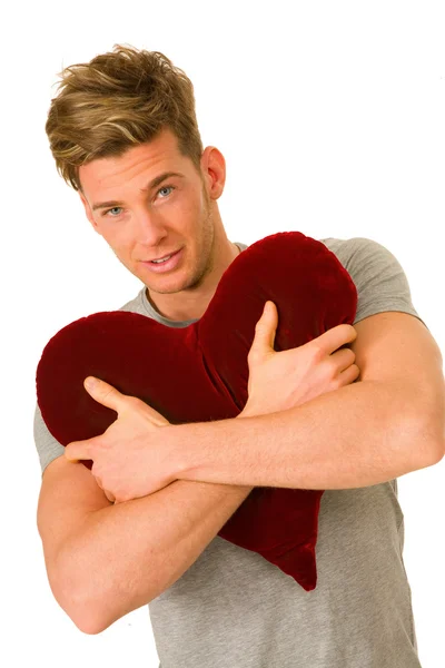 Νεαρός άνδρας αγκαλιάζει ένα σχήμα καρδιάς μαξιλάρι — Φωτογραφία Αρχείου