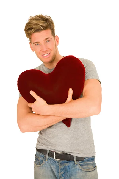Νεαρός άνδρας αγκαλιάζει ένα σχήμα καρδιάς μαξιλάρι — Φωτογραφία Αρχείου