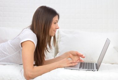 Woman lying on a sofa with laptop paying bills online clipart