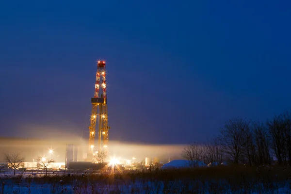 Pozo de petróleo en el campo iluminado por la noche . — Foto de Stock