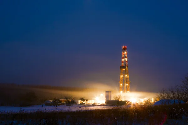 Oil well in the snowy landscape lit up at night. — Stock Photo, Image
