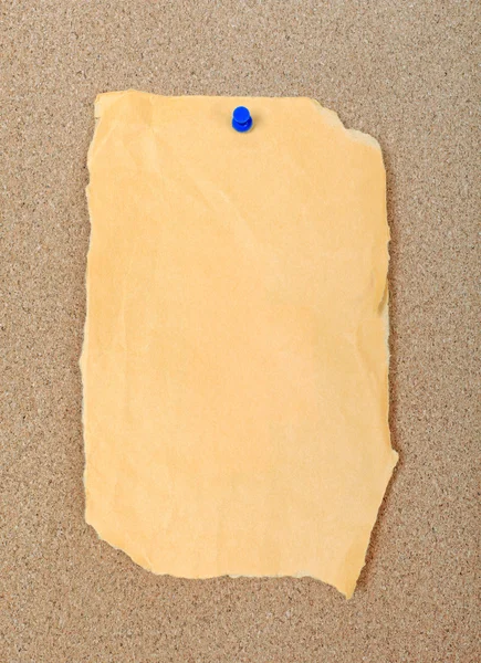 A piece of empty torn paper attached with blue pin to cork messa — Stock Photo, Image
