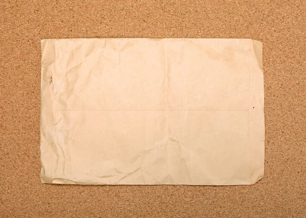 Wrinkled brown envelope attached to cork board. As backdrop or b — Stock Photo, Image