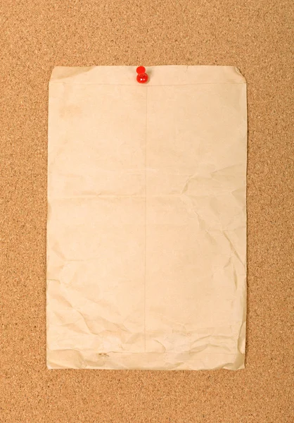 Wrinkled brown envelope attached to cork board with red pin. Emp — Stock Photo, Image