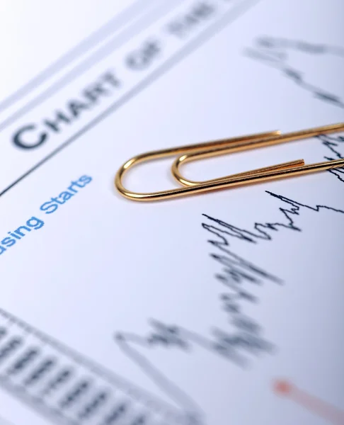 Golden paperclip laying on financial chart. — Stock Photo, Image