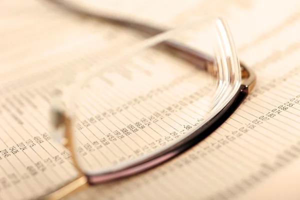 Macro of financial data through eyeglasses, laying on newspaper. — Stock Photo, Image